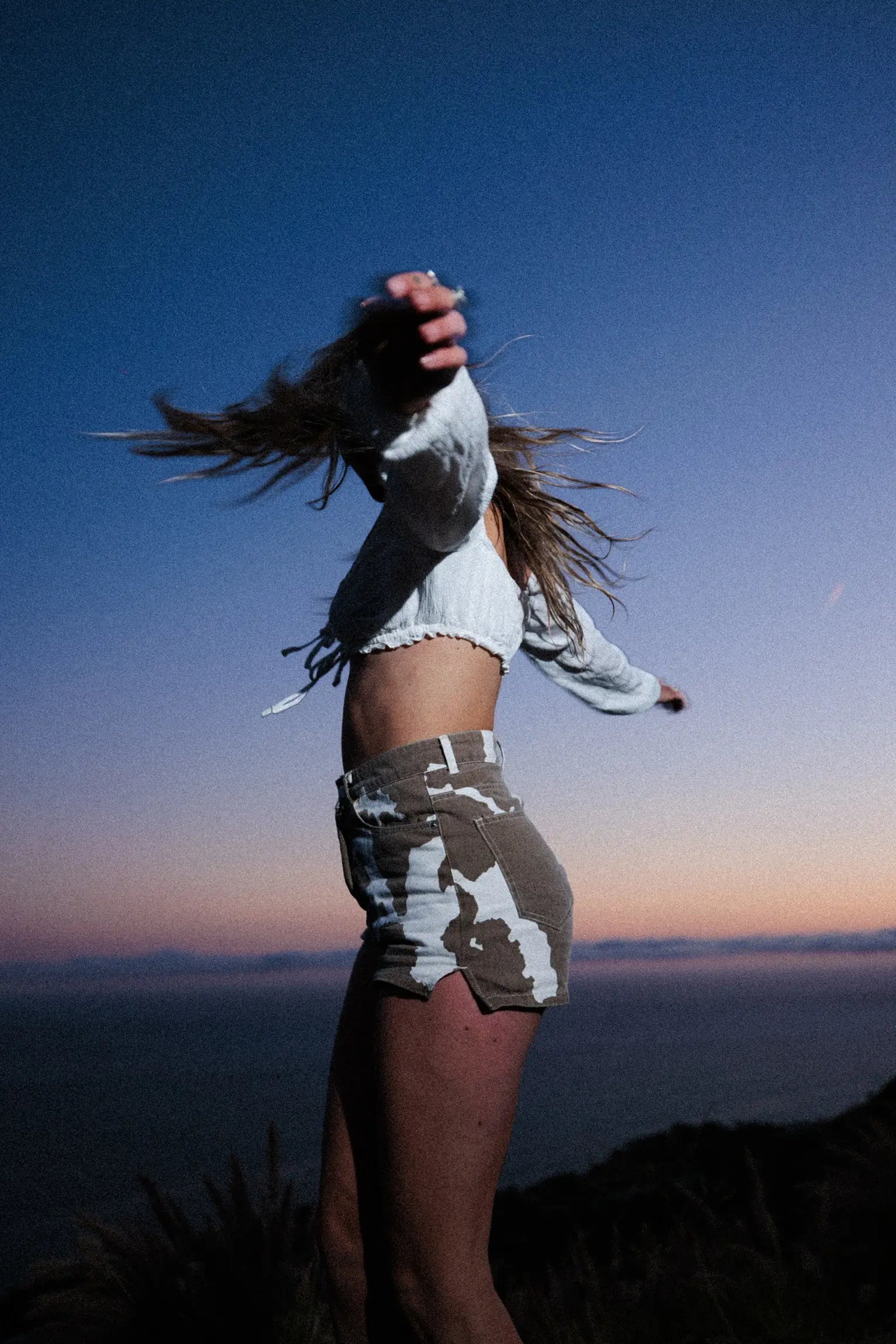 Woman spinning at sunset with ocean in the background.